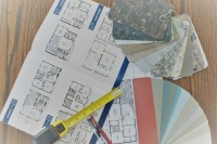 A photo of an home blueprint, color samples, and a measuring tape on a wooden table.